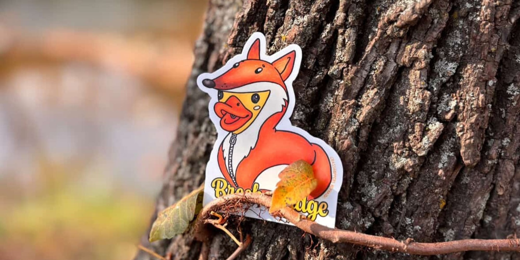 A sticker of a duck wearing a fox costume placed on a tree trunk, with the text "Breckenridge" at the bottom.